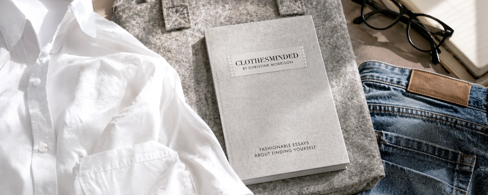 Flat lay of Clothes Minded by Christine Morrison styled with a white shirt, denim jeans, glasses, and notebook in a soft editorial setting.