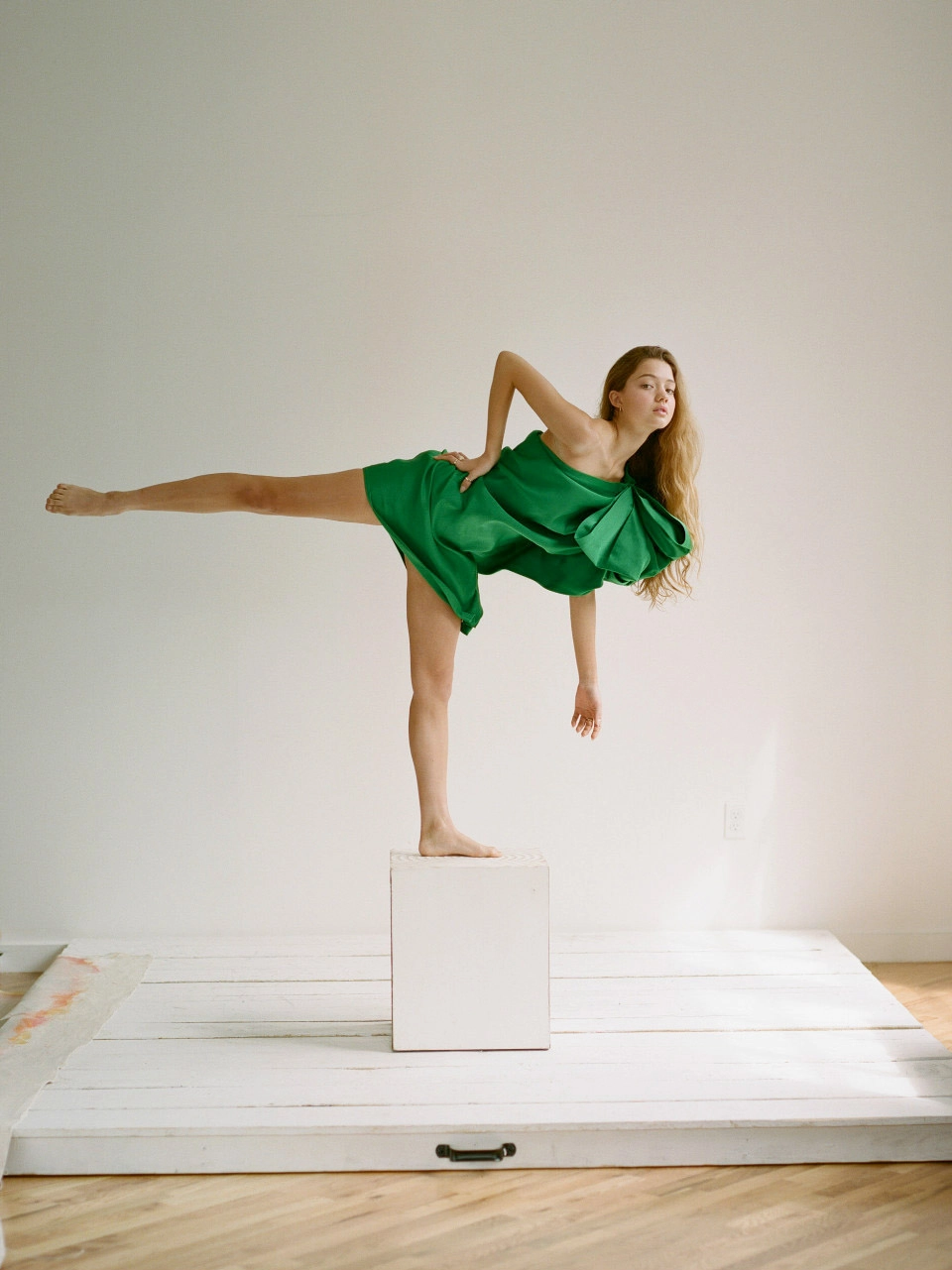 Ruby Snowber balances on a pedestal in an emerald-green dress during a fashion editorial photoshoot for Ebby Magazine.