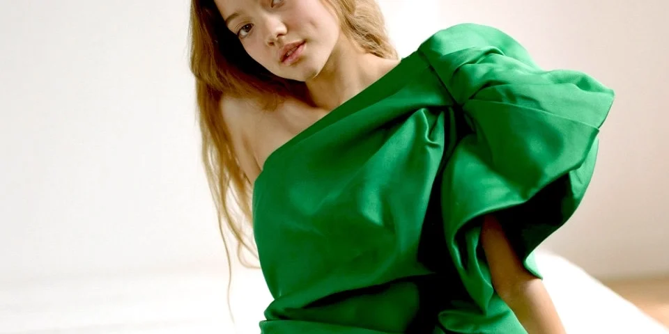 Ruby Snowber poses in a sculptural emerald-green gown, showcasing modern fashion and effortless elegance in a studio portrait.