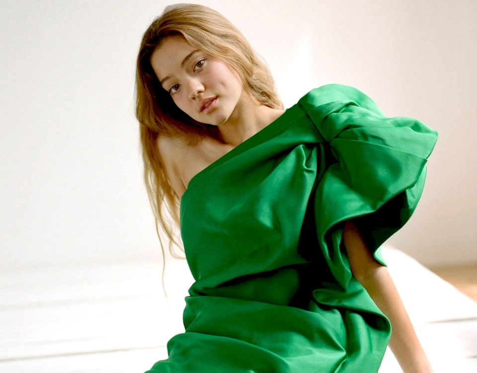 Ruby Snowber poses in a sculptural emerald-green gown, showcasing modern fashion and effortless elegance in a studio portrait.