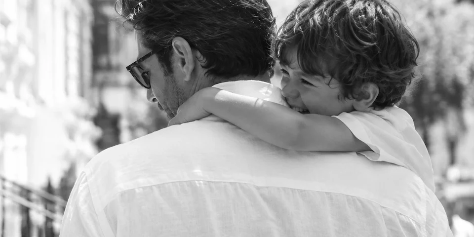 Father carrying smiling child on his shoulders in a candid black-and-white Father’s Day lifestyle photo