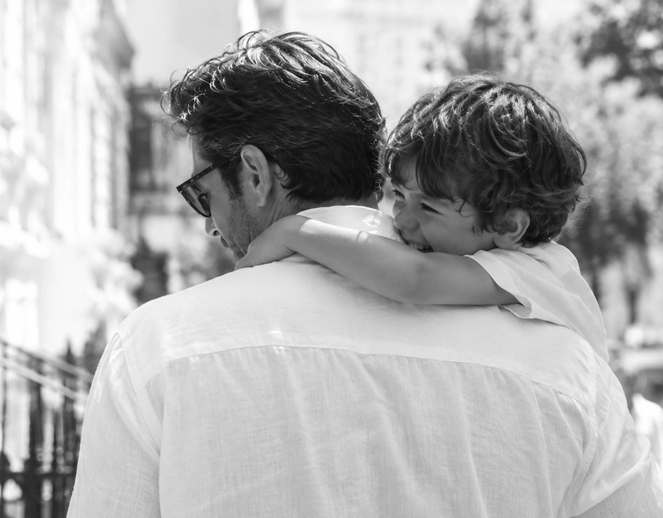 Father carrying smiling child on his shoulders in a candid black-and-white Father’s Day lifestyle photo