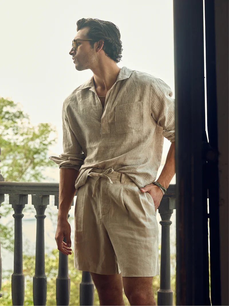 an wearing a beige linen shirt and tailored shorts in a luxury summer menswear editorial.