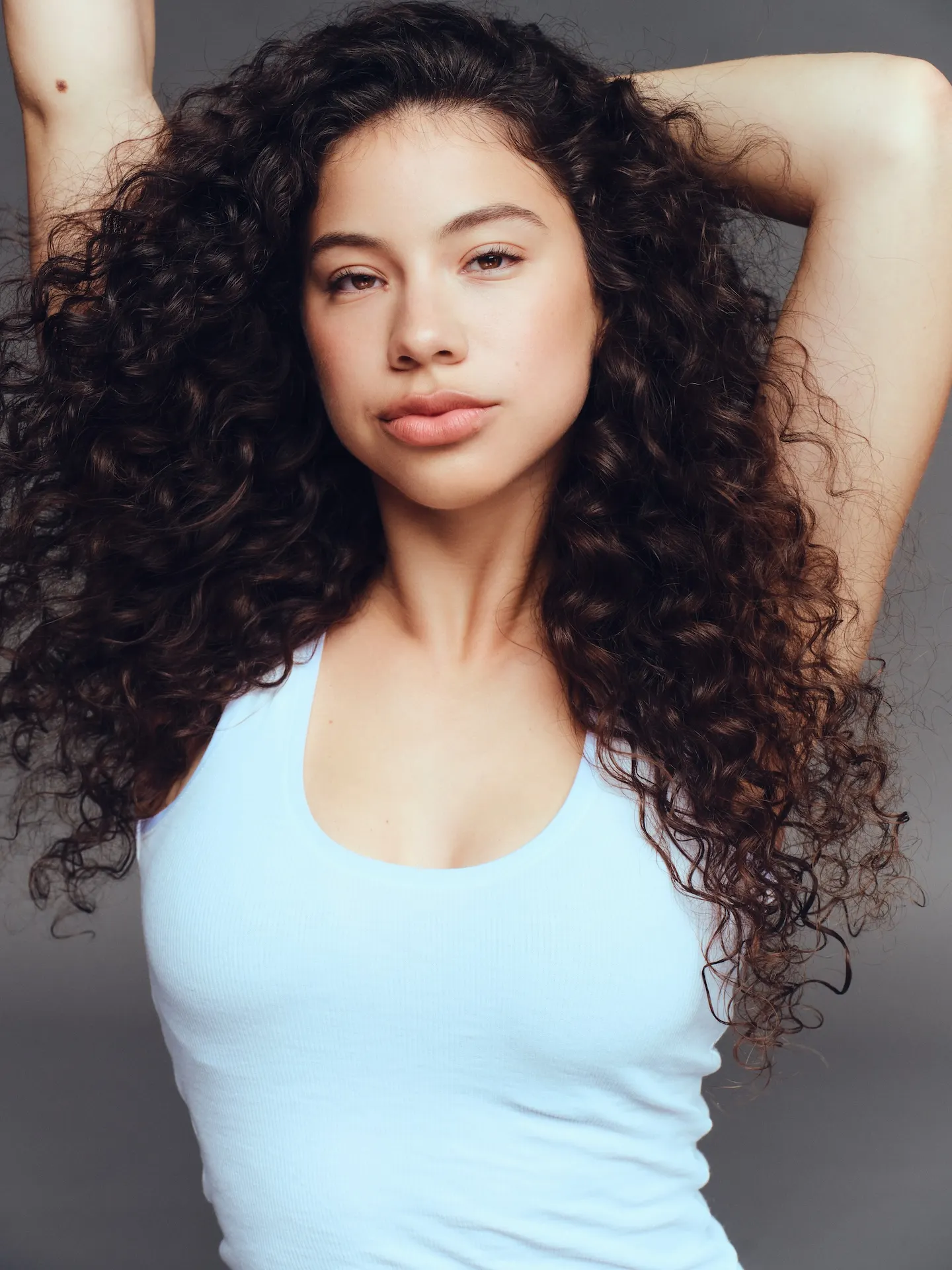 Actress Kiara Romero wearing a blue tank top with her hands raised behind her head.